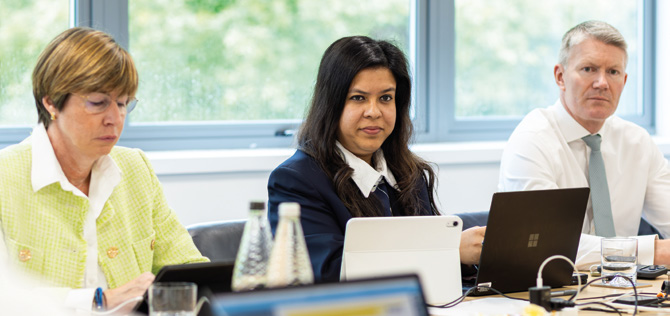 Board members around a conference table — three directors with laptops